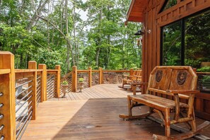 Un patio in legno con ringhiera, panchine e vista sulla foresta.