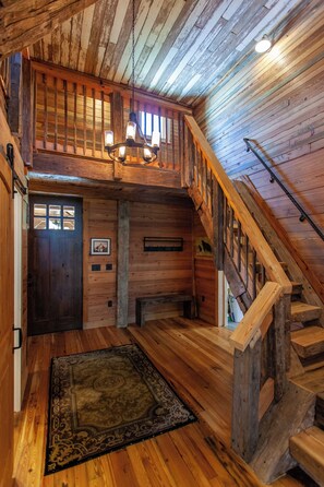 A wooden interior with a staircase, a chandelier, and a rug. - Castle Rock Luxury Cabin with Smoky Mt Views (Bryson City)