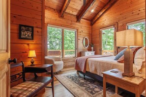 A wooden cabin bedroom with a bed, two chairs, a desk, and a dresser. - Castle Rock Luxury Cabin with Smoky Mt Views (Bryson City)