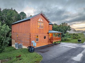 A log cabin with a porch, a small attached structure, and a paved driveway. - 84° Indoor Pool, 75” TV, Hot Tub, Air Hockey, WIFI, Arcade, A+ Location (Pigeon Forge)