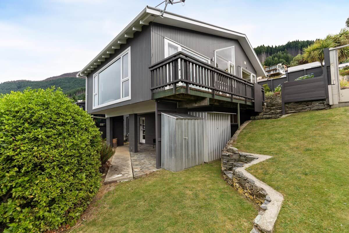 A modern two-story house with a balcony, a stone retaining wall, and a well-maintained lawn.