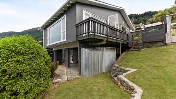 A modern two-story house with a balcony, a stone retaining wall, and a well-maintained lawn.