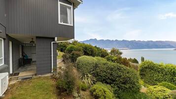A modern two-story house with a balcony overlooking a lake and mountains.