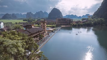 A riverside hotel with a dock, buildings, and a mountainous backdrop.