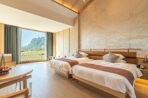 A hotel room with two beds, a dining table, and a large window with a view of mountains. - chongzuo longzhou guantang jiudian (Chongzuo)