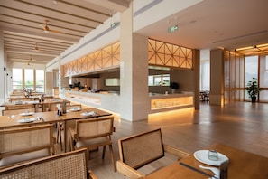 A spacious dining area with wooden tables and chairs, a central counter, and large windows allowing natural light.