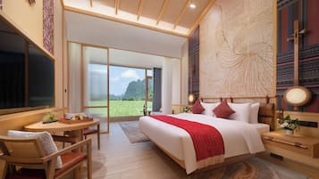A modern bedroom with a large bed, a dining area with a table and chairs, and a view of a green field through the window.