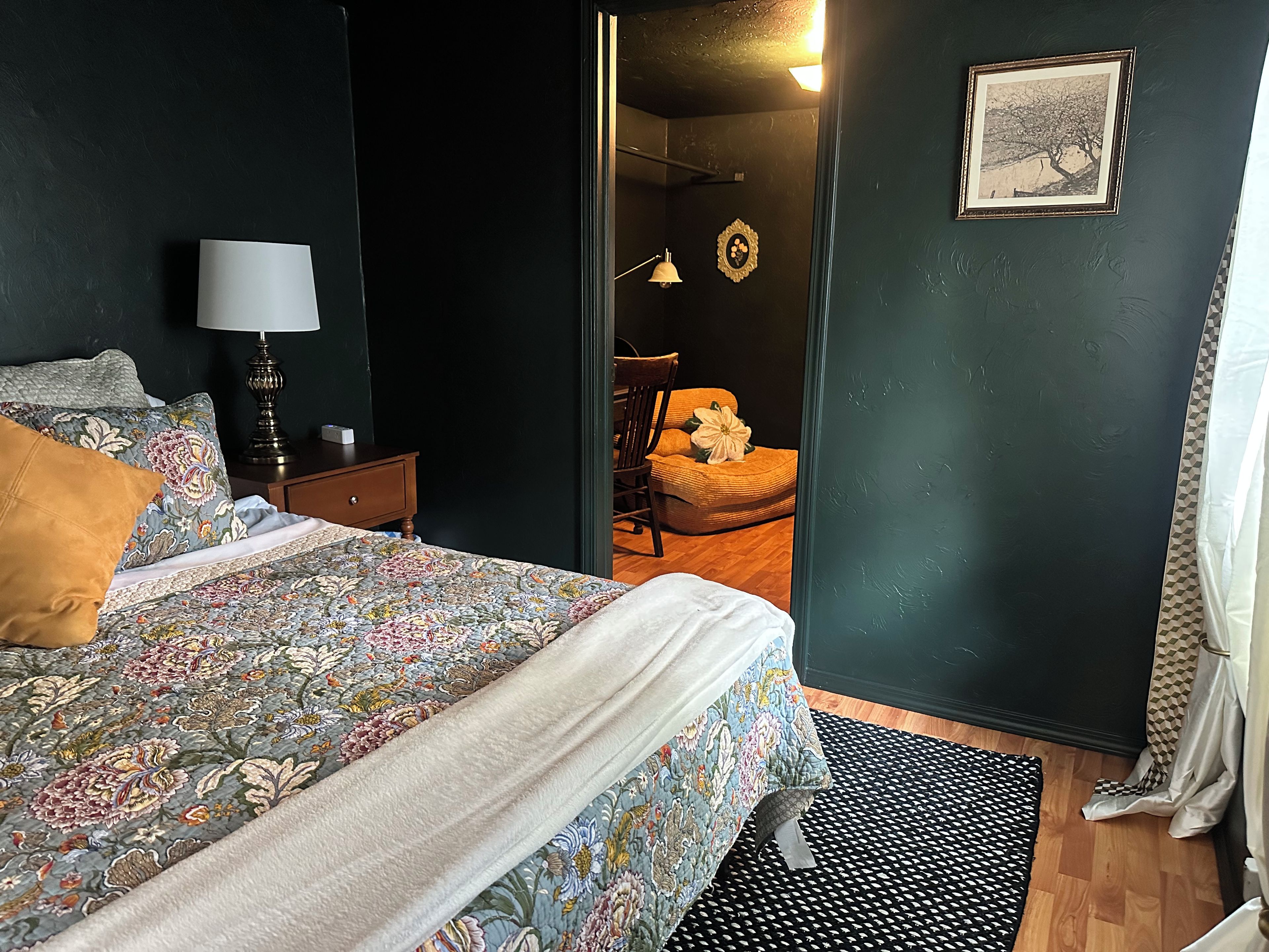 A bedroom with a bed, a nightstand, a lamp, a chair, and a door leading to another room.