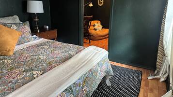 A bedroom with a bed, a nightstand, a lamp, a chair, and a door leading to another room.