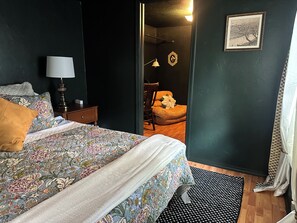 A bedroom with a bed, a nightstand, a lamp, a chair, and a door leading to another room.