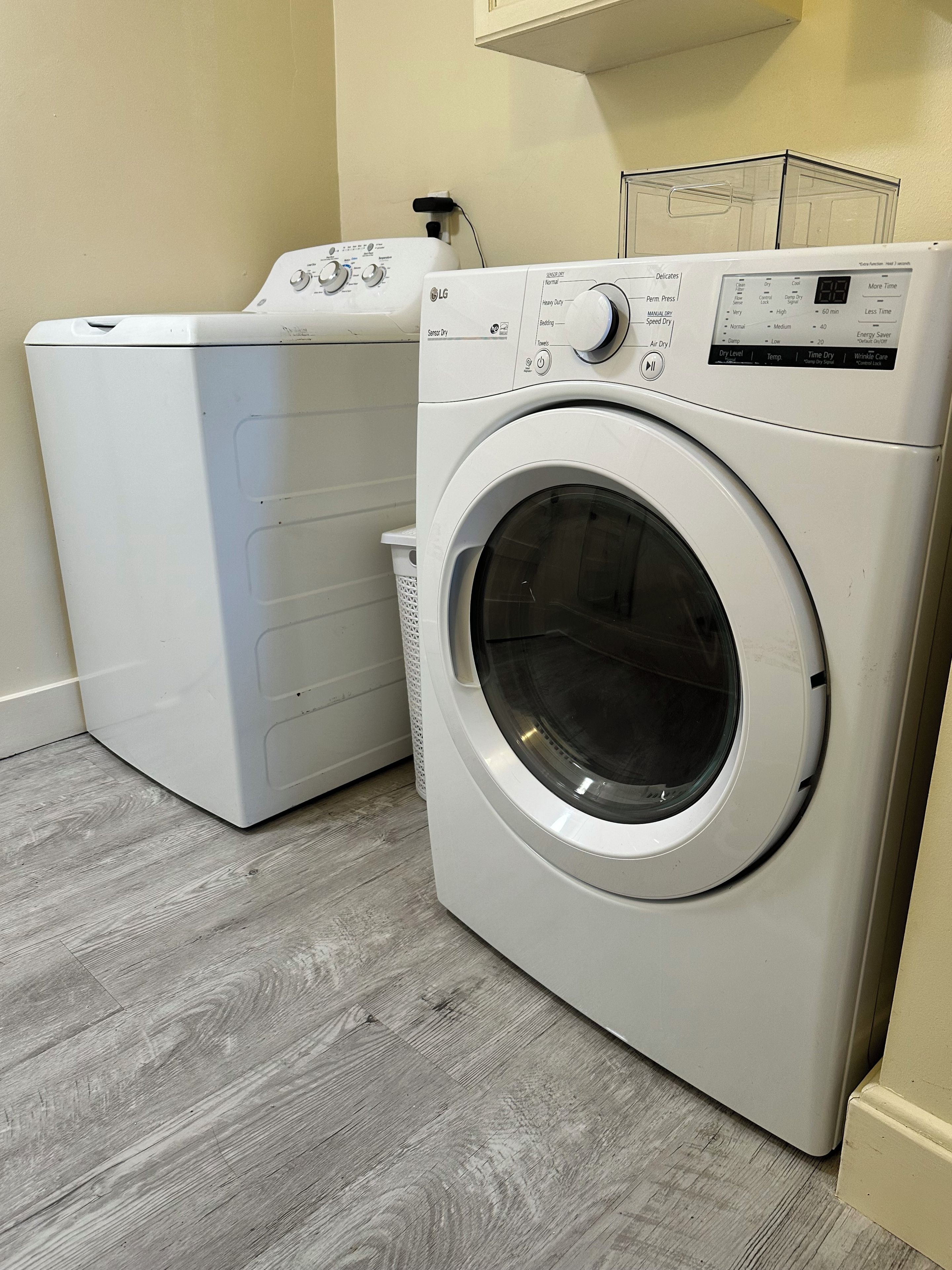 A front-loading washing machine and dryer in a laundry room with a wooden floor.