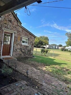 A stone house with a brown door, a small front porch, and a brick pathway leading to the entrance.