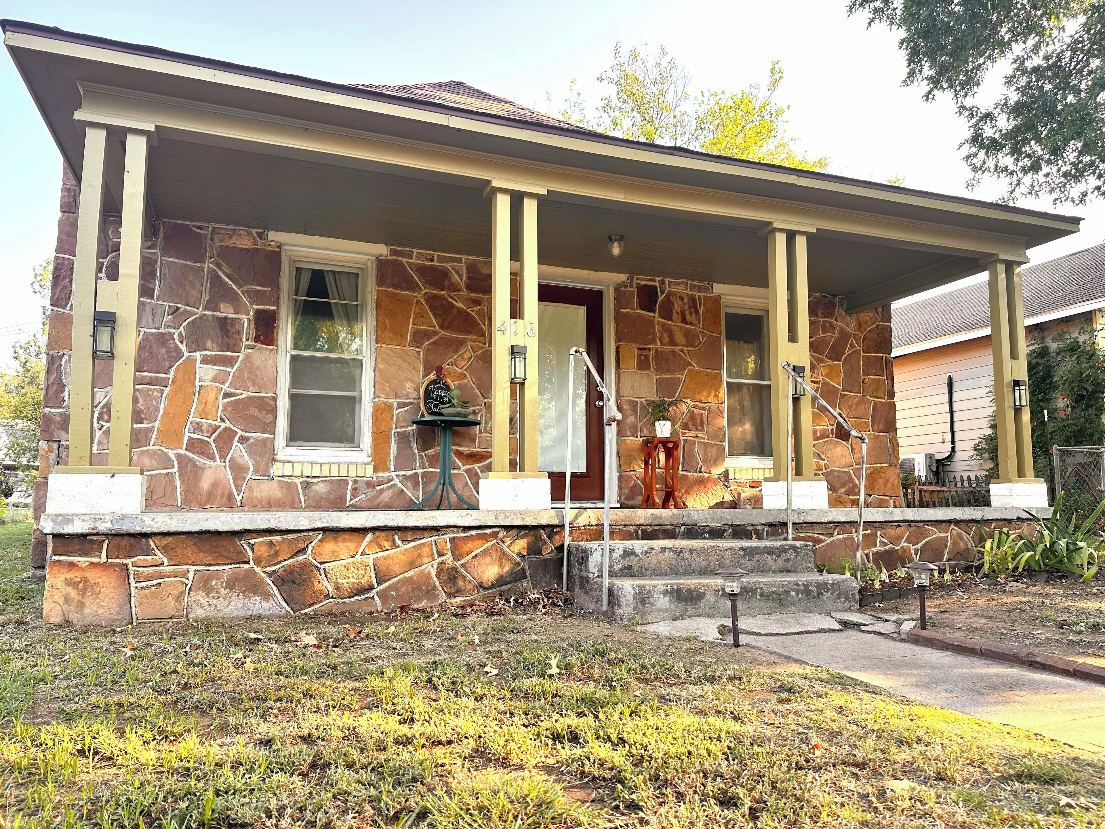 A stone house with a porch, a mailbox, and a small table with a potted plant.