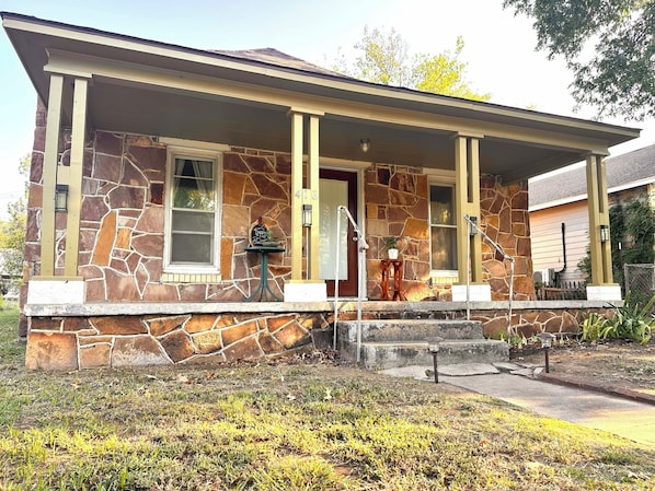 A stone house with a porch, a mailbox, and a small table with a potted plant.