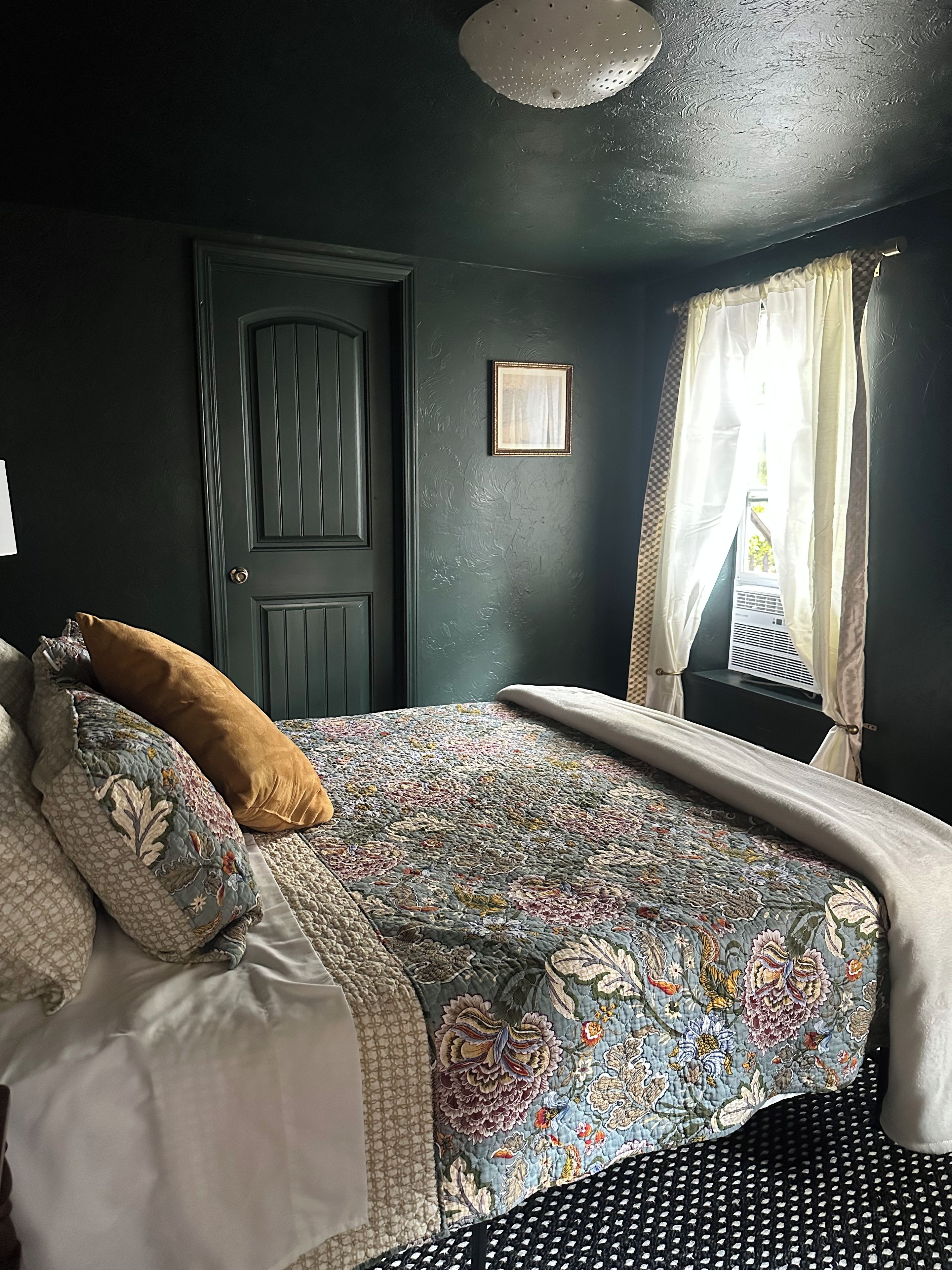 Une chambre avec un mur vert foncé, une couvre-lit à motifs et une porte ornée d’un motif en losanges.