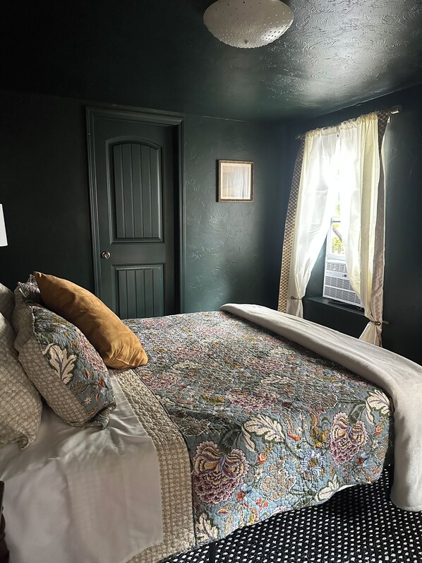 A bedroom with a dark green wall, a patterned bedspread, and a door with a diamond pattern.
