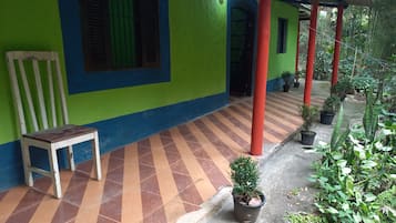A covered outdoor area with a bench, potted plants, and a tiled floor.