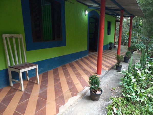 A covered outdoor area with a bench, potted plants, and a tiled floor.