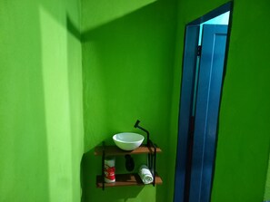 Et badeværelse med grøn væg, en hvid skål på en hylde, toiletpapir og en blå dør.