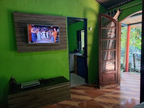 A room with a television mounted on a wall, a wooden cabinet, and a door leading to an outdoor area.