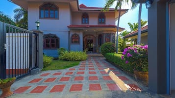 A two-story house with a covered entrance, a paved driveway, and a gated entrance.