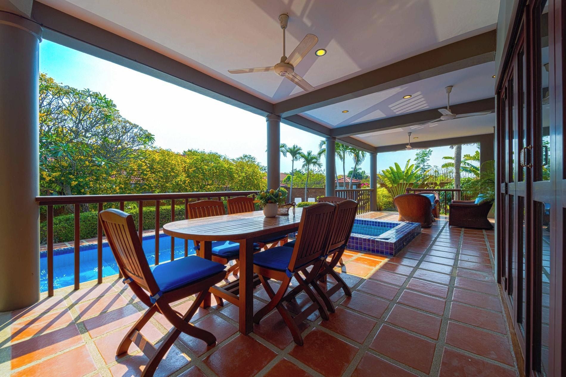 A covered outdoor area with a pool, seating, and a view of greenery.