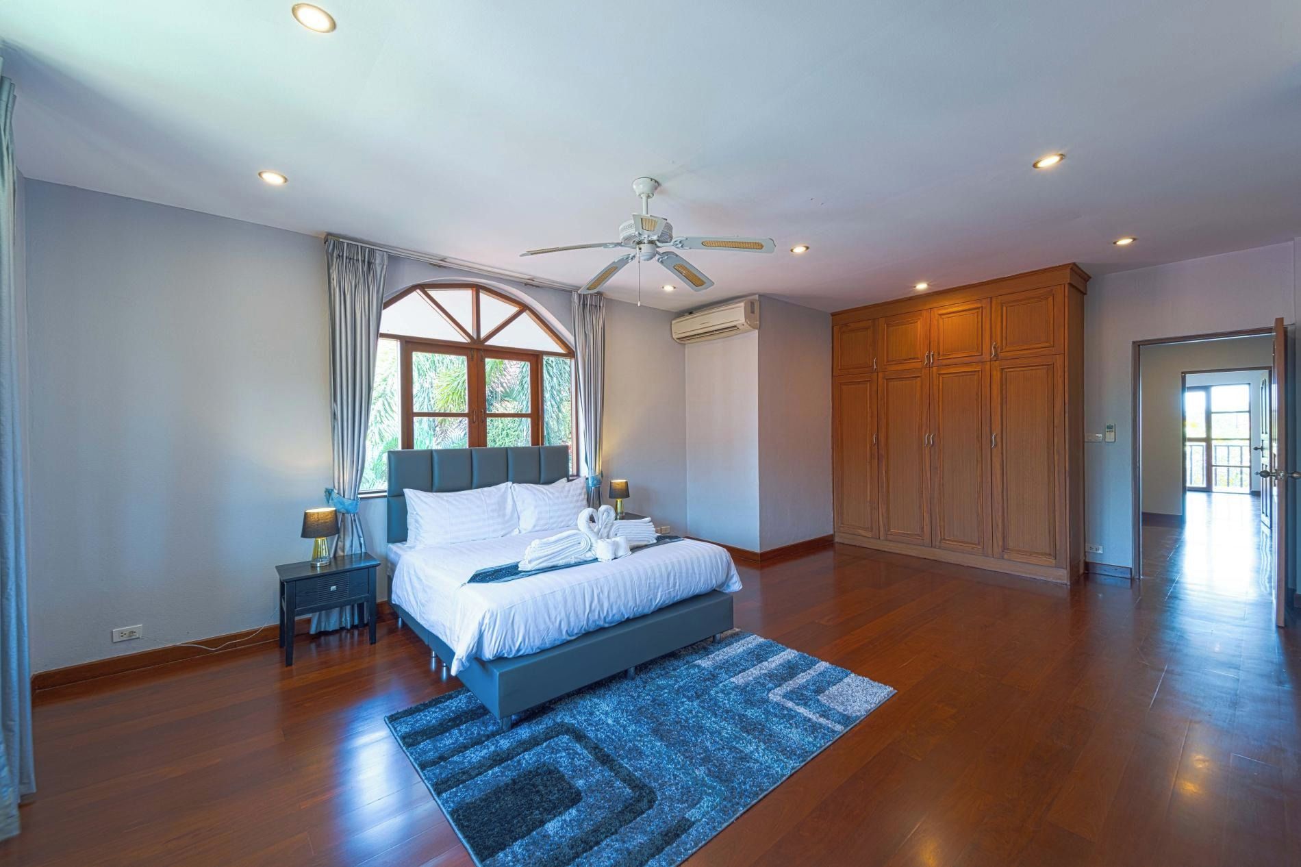 A spacious bedroom with a large bed, a ceiling fan, and a view through a window.
