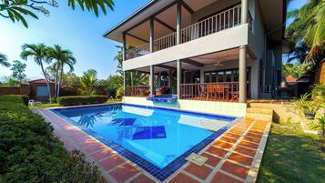 A modern two-story building with a swimming pool, outdoor seating, and lush greenery.