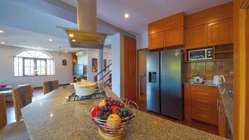 Una cocina con encimeras de granito, un refrigerador de acero inoxidable, armarios de madera y un frutero en la isla.