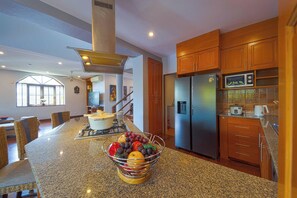Una cocina con encimeras de granito, un refrigerador de acero inoxidable, armarios de madera y un frutero en la isla.