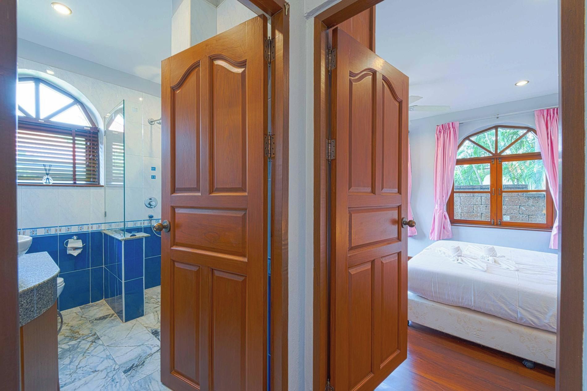 Una habitación con cama, baño con lavamanos y espejo, y ventana con cortinas.