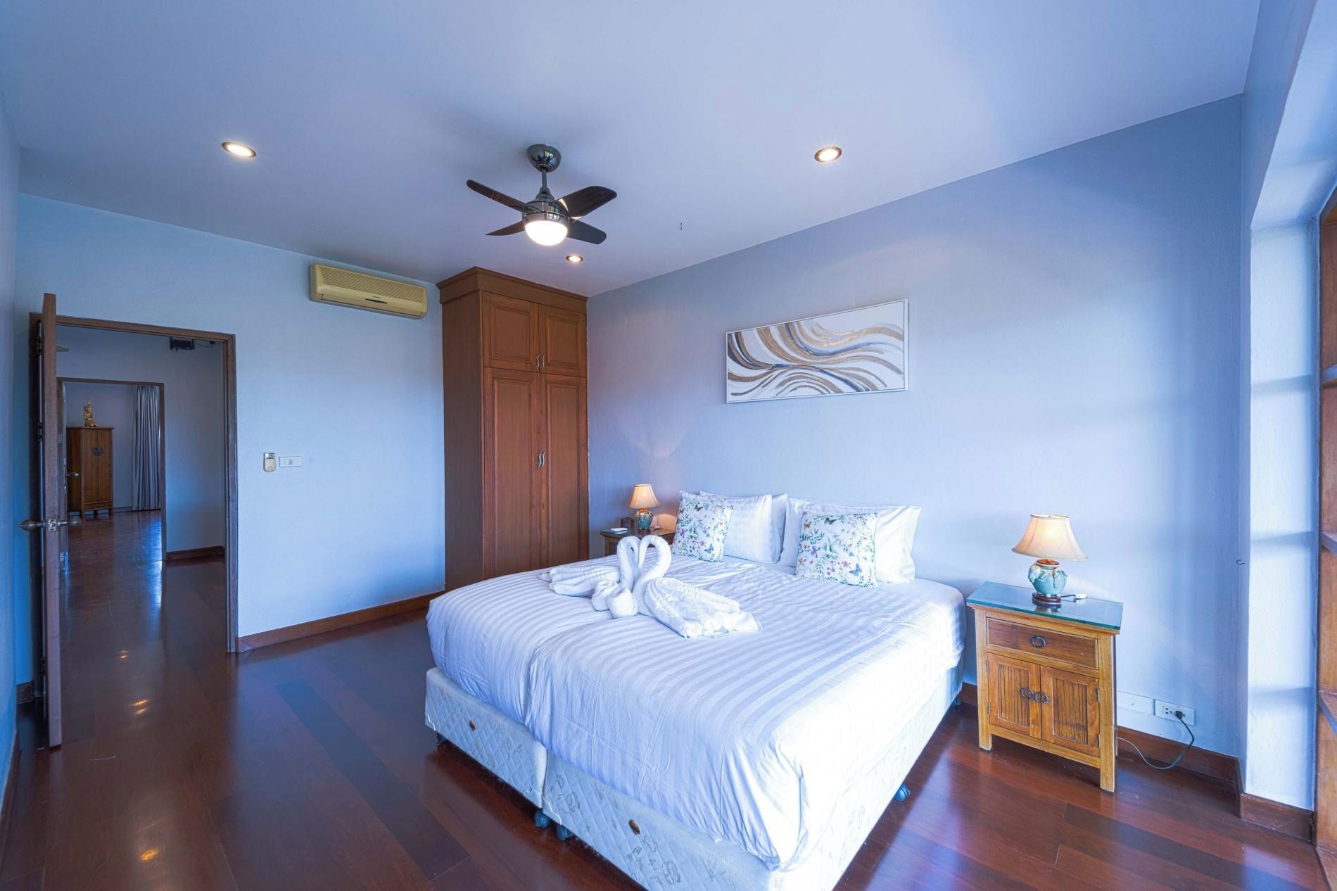 Une chambre à coucher avec un grand lit, un ventilateur de plafond, une armoire en bois et une table de chevet avec une lampe.