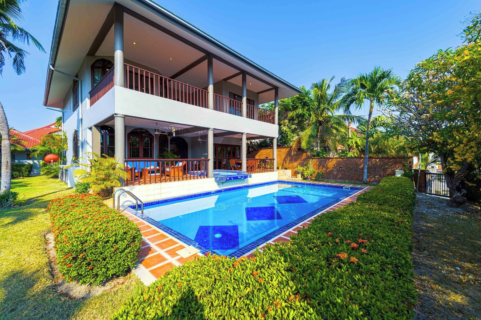 Uma casa de dois andares com piscina, rodeada por vegetação e palmeiras.