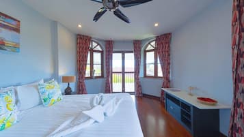 A hotel room with a bed, a desk, a ceiling fan, and large windows with curtains.