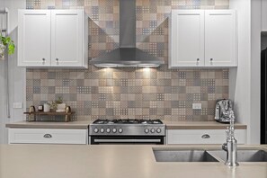 Een keuken met witte kastjes, een roestvrijstalen afzuigkap en een decoratieve achterwand.