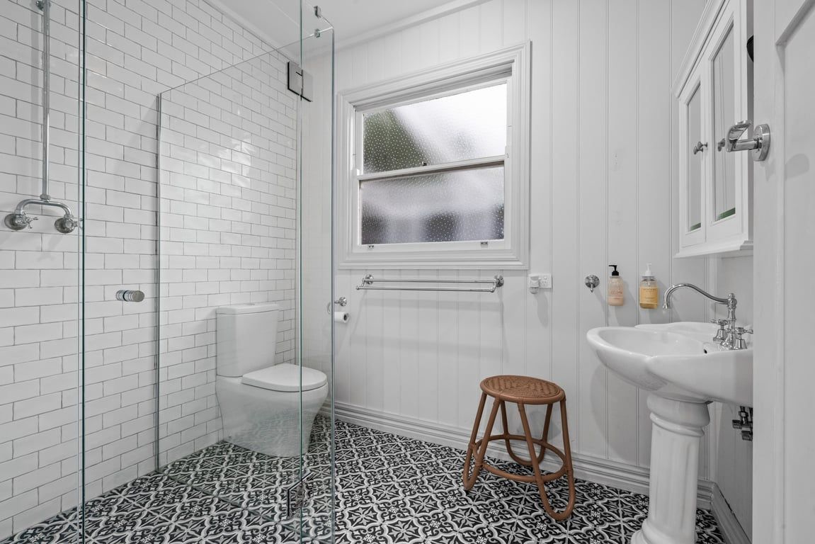 A bathroom with a glass shower enclosure, a toilet, a sink, and a window.
