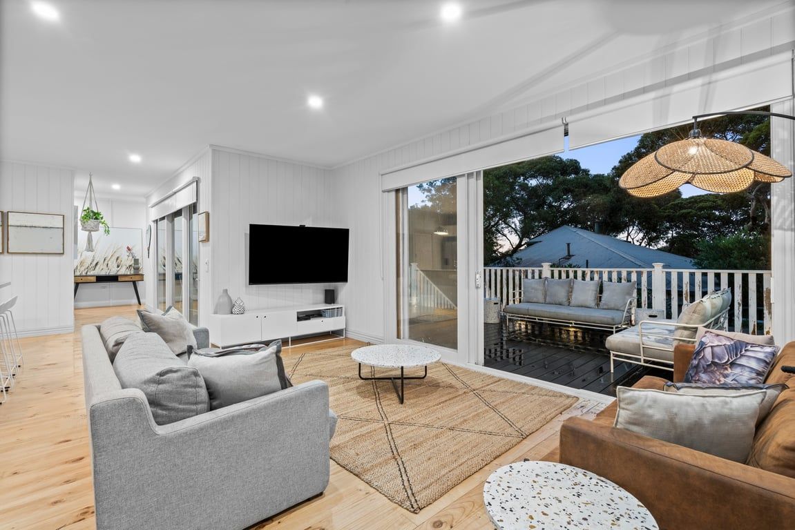 A modern living room with a flat-screen TV, grey sofas, a coffee table, and a balcony with outdoor seating.