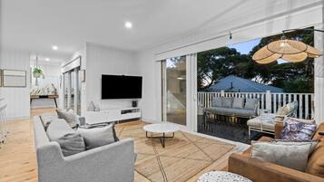 A modern living room with a flat-screen TV, grey sofas, a coffee table, and a balcony with outdoor seating.