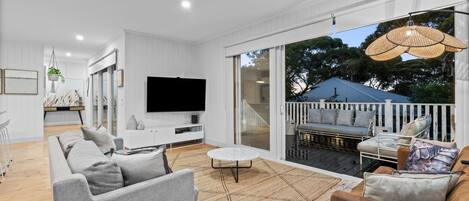 En moderne stue med et fladskærms-tv, grå sofaer, et sofabord og en balkon med udendørs møbler.