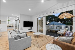 Ein modernes Wohnzimmer mit Fernseher, grauen Sofas, einem Couchtisch und einem Balkon mit Sitzgelegenheit.