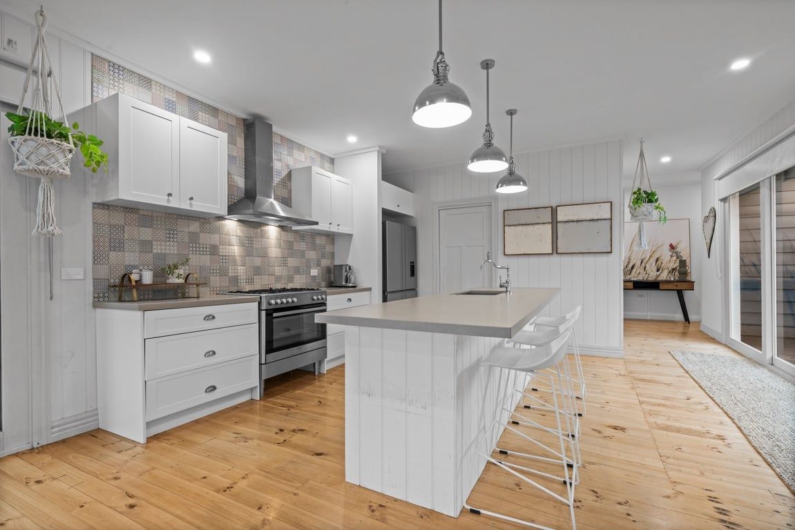 A modern kitchen with white cabinetry, a central island, hanging pendant lights, and a wooden floor.