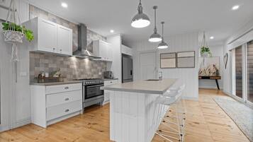 A modern kitchen with white cabinetry, a central island, hanging pendant lights, and a wooden floor.