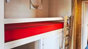 Een stapelbed met een rode matras, een houten trapje en een deur aan de rechterkant.