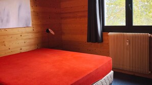 Een kamer met een bed, een radiator, een raam met gordijnen en een wandlamp.