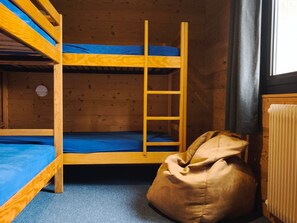 Dormitorio con literas, un sillón de mimbre y un radiador.