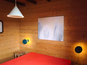 Una habitación con paredes de madera, una cama con cubierta roja, una lámpara de techo blanca y dos lámparas de pared.