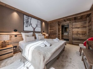 A modern bedroom with a large bed, wooden headboard, a wall-mounted artwork, and a visible bathroom door. - Chalet at the foot of the slopes, pets OK - 8 guests (Courchevel 1550)