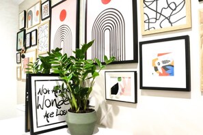 Eine Wand mit mehreren gerahmten Kunstwerken und einem Blumentopf mit einem motivierenden Zitat.