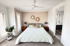 Un dormitorio con una cama, dos mesitas de noche, un ventilador de techo y una planta en maceta.