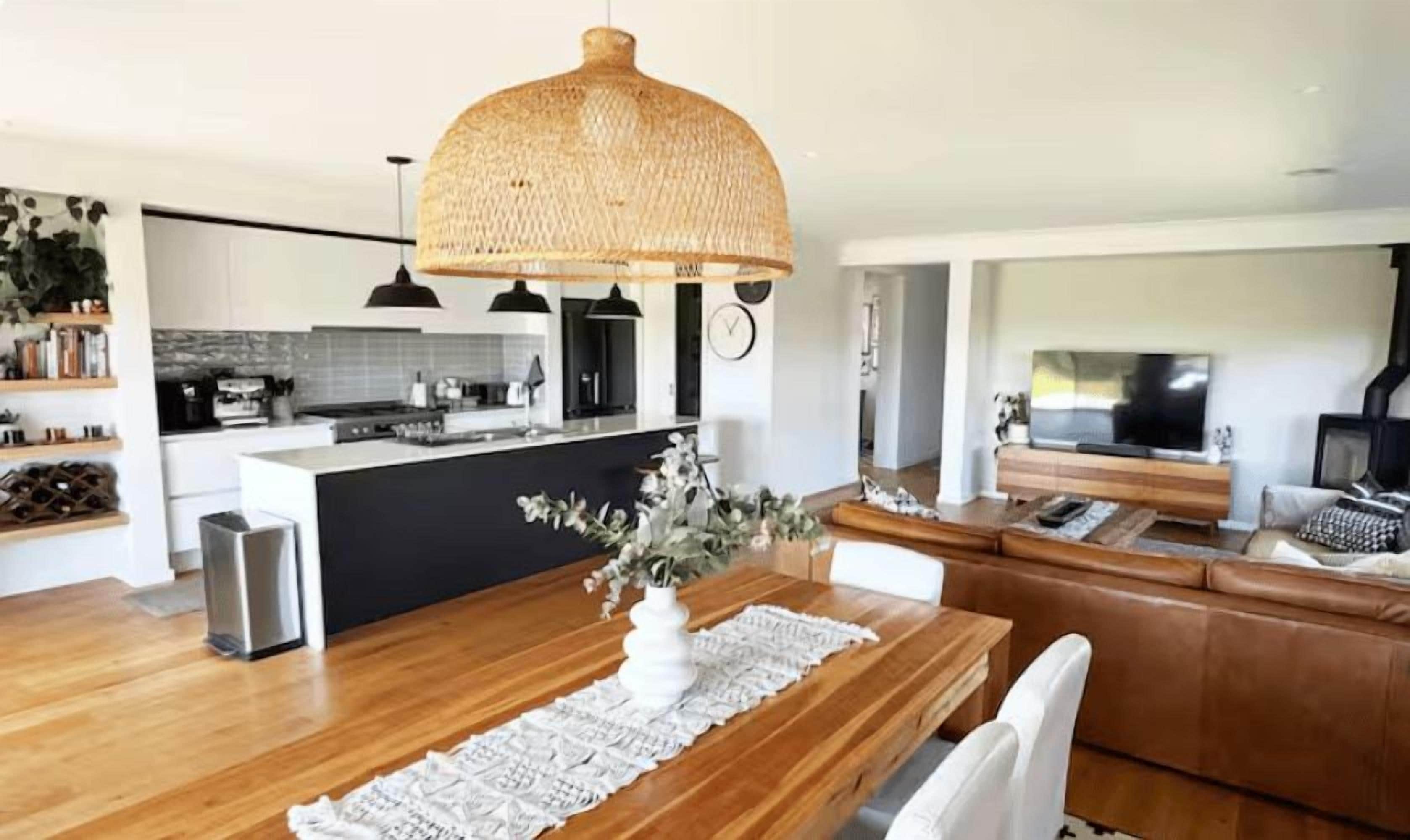 A modern kitchen with a central island, a dining area with a wooden table and white runner, and a cozy seating area with a sofa and a TV.
